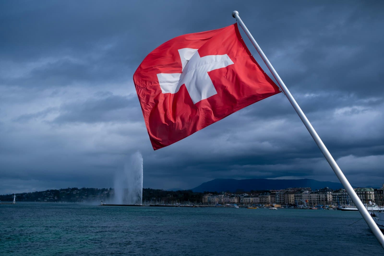 A Swiss flag flying over Lake Geneva under a stormy sky